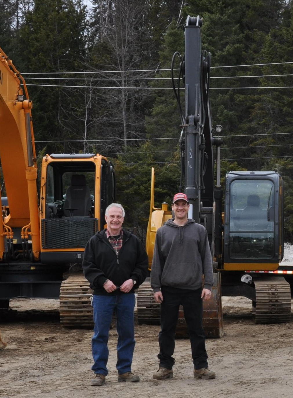 L'équipe de la compagnie Excavation M.Ayotte et Fils. Robert Ayotte a la gauche et David Ayotte a la droite. En arrière plan, trois pelles mechanics (grosse, moyenne, et petite) et un dix roues.